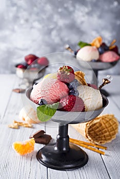 Bowl with ice cream with three different scoops of white, yellow, red colors and waffle cone, chocolate, tangerines and