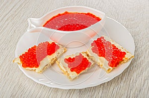 Bowl with imitation salmon caviar, pieces of crispbread with butter and caviar in plate on wooden table