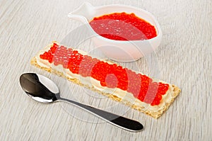 Bowl with imitation salmon caviar, sandwich with butter and caviar, spoon on wooden table