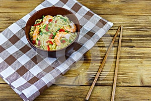 Bowl of instant Chinese noodles with shrimps, green onion and red hot chilli peppers on wooden table