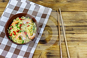 Bowl of instant Chinese noodles with shrimps, green onion and red hot chilli peppers on wooden table. Top view