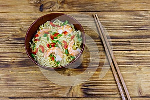 Bowl of instant Chinese noodles with shrimps, green onion and red hot chilli peppers on wooden table. Top view