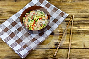 Bowl of instant Chinese noodles with shrimps, green onion and red hot chilli peppers on wooden table. Top view