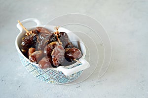 Bowl with juicy dates on a branch on a gray-blue background. Healthy tasty food. Raw Dates
