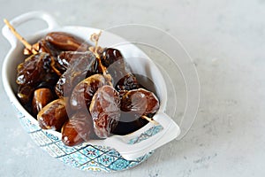 Bowl with juicy dates on a branch on a gray-blue background. Healthy tasty food. Raw Dates