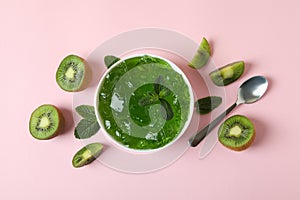 Bowl of kiwi jelly, kiwi slices, spoon and mint on pink background