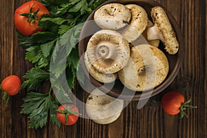 A bowl with large wild mushrooms, vegetables and celery leaves on a wooden table. Flat lay