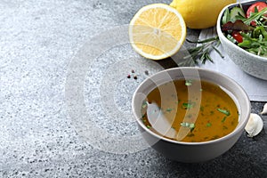 Bowl with lemon dressing near salad on grey table, space for text. Delicious salad dressing