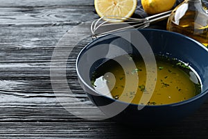 Bowl with lemon sauce on black wooden table, space for text. Delicious salad dressing