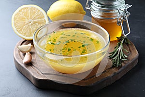 Bowl with lemon sauce and ingredients on dark table. Delicious salad dressing