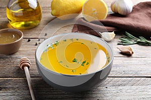 Bowl with lemon sauce and ingredients on wooden table. Delicious salad dressing