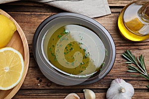 Bowl with lemon sauce and ingredients on wooden table, flat lay. Delicious salad dressing