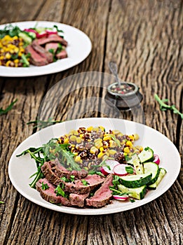 Bowl lunch with grilled beef steak and quinoa, corn, cucumber, radish and arugula