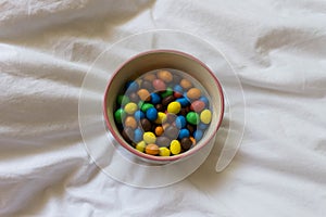 Bowl of M&M`s in a bed. Disconnection moment on the bed. Self care concept. Rest and enjoy moment