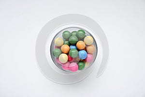 Bowl with many bright gumballs on white background, top view