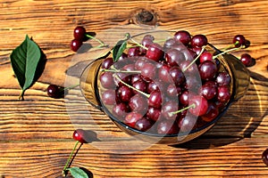 A bowl with many cherries stands on a wooden background.