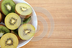 Bowl of many cut fresh kiwis on wooden table, top view. Space for text