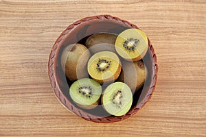 Bowl with many whole and cut fresh kiwis on wooden table, top view