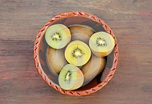 Bowl with many whole and cut fresh kiwis on wooden table, top view