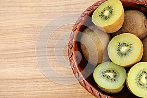 Bowl of many whole and cut fresh kiwis on wooden table, top view. Space for text