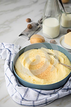 Bowl with mashed potatoes and ingredients as potato, milk, salt, butter, nutmeg with kitchen towel and grinder on light marble