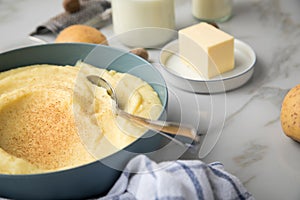 Bowl with mashed potatoes and ingredients as potato, milk, salt, butter, nutmeg with kitchen towel and grinder on light marble