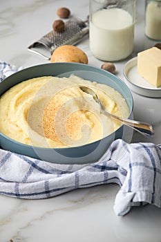 Bowl with mashed potatoes and ingredients as potato, milk, salt, butter, nutmeg with kitchen towel and grinder on light marble