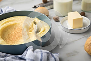 Bowl with mashed potatoes and ingredients as potato, milk, salt, butter, nutmeg with kitchen towel and grinder on light marble