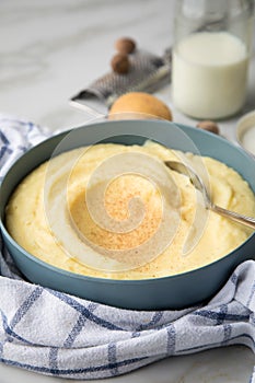Bowl with mashed potatoes and ingredients as potato, milk, salt, butter, nutmeg with kitchen towel and grinder on light marble