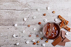 Bowl of melted milk chocolate with hazelnuts on a wooden table