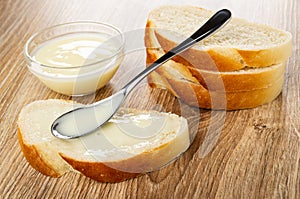 Bowl with milk, spoon on sandwich with condensed milk, slices of bread on wooden table