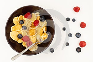 A bowl with mini pancake cereal. Tiny cereal pancakes with blueberries and raspberries