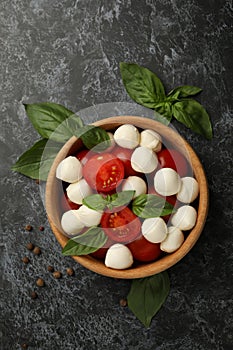 Bowl with mozzarella cheese, tomato and basil on black smokey background, top view