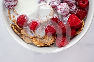 Bowl of multigrain cereal with yogurt and fresh raspberry berries on marble table background. Healthy diet breakfast.