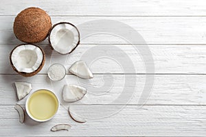 Bowl of natural organic oil and coconuts on white wooden background, flat lay