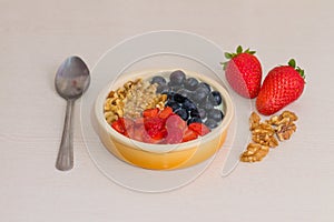 Bowl with natural yogurt and fresh fruits on wooden white table. Strawberries, blueberries and nuts with selective focus.