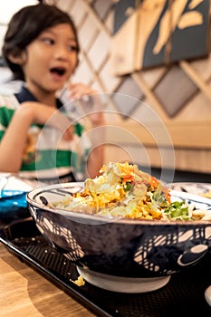 A bowl of noodle menu served at Japanese restaurant, with a happy little Asian boy in the background