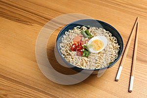 Bowl of noodles with broth, egg, vegetables and chopsticks served on wooden table.