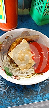 A bowl noodles with chili sauce and chips