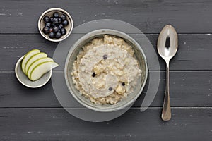 A bowl of nutritious blueberry and apple porridge and a small bowl of  apple and blueberries, with a spoon, on a dark wooden