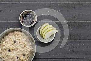 A bowl of nutritious blueberry and apple porridge and a small bowl of blueberries and apple, on a dark wooden background, with