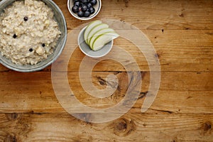 A bowl of nutritious blueberry and apple porridge and a small bowl of blueberries and apple, on a wooden background, withcopy