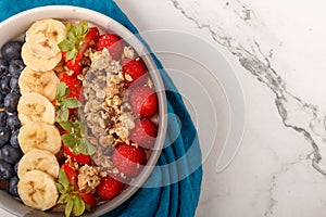 Bowl of oat granola with yogurt, fresh raspberries, blueberries, strawberries, banana and nuts