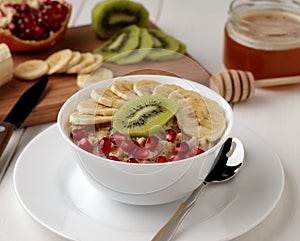 Bowl of oatmeal with banana, kiwi, garnet and honey.