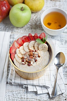 Bowl of oatmeal with a banana, strawberries, almonds, hazelnuts and butter on a rustic table. Hot and a healthy dish for Breakfast