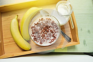 Bowl of oatmeal chocolate flakes in the shape of letters of the alphabet with milk on a wooden tray with bananas and a jug of milk