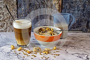 A bowl of oatmeal and nuts. Next to it is a glass of latte macchiato and a jug of milk