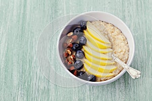 Bowl of oatmeal porridge with apple, berries, honey and almond on rustic table, diet breakfast