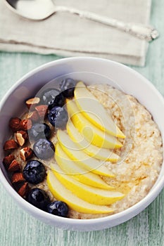 Bowl of oatmeal porridge with apple, berries, honey and almond on rustic table, diet breakfast