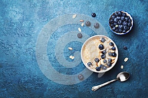 Bowl of oatmeal porridge with banana and blueberry on vintage table top view in flat lay style. Healthy breakfast and diet food.